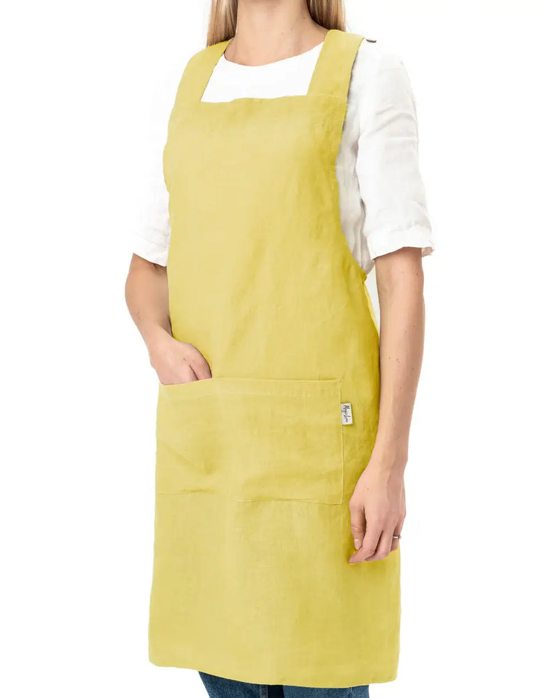 MagicLinen - Pinafore cross-back linen apron, worn by a woman, featuring a twin-sectioned front pocket and durable design for cooking and gardening.