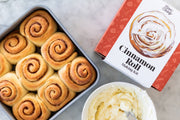 FarmSteady - Cinnamon Roll Making Kit with un-iced rolls, icing bowl, and branded box, showcasing homemade cinnamon delights for a delicious baking experience.
