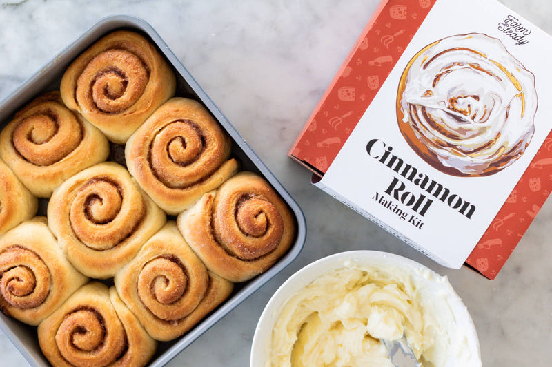 FarmSteady - Cinnamon Roll Making Kit with un-iced rolls, icing bowl, and branded box, showcasing homemade cinnamon delights for a delicious baking experience.
