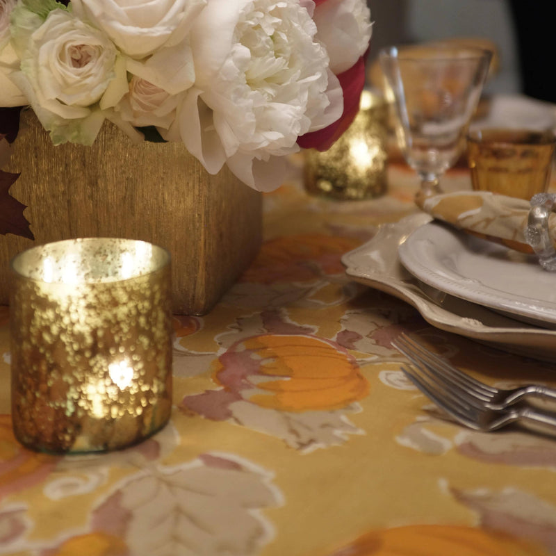 Autumn-themed table with Caravan Home - Pumpkin Orange & Mustard Tablecloth, gold vase, votive, and cream plates, reflecting Couleur Nature's artisanal craftsmanship.