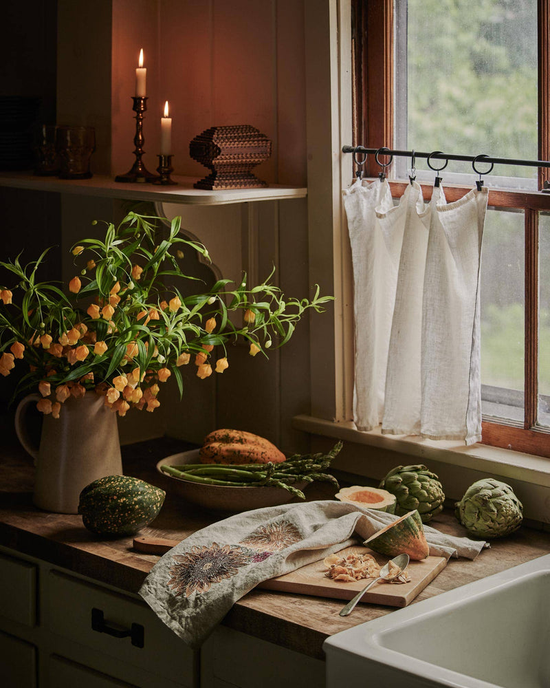 Coral & Tusk - Autumn Sunflower Tea Towel draped over a cutting board with squash, artichokes, asparagus, and a rustic kitchen setup, showcasing seasonal kitchen elegance.