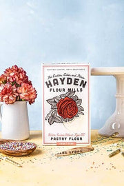 Hayden Flour Mills - Pastry Flour box with rose design, set among festive confetti, sprinkles, flowers, and cake stand, ideal for sophisticated baking.