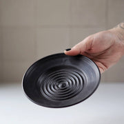 Gravesco Pottery - Garlic Grater Plate in Black, hand holding a matte-black ceramic dish with concentric ridges, ideal for garlic preparation and serving.