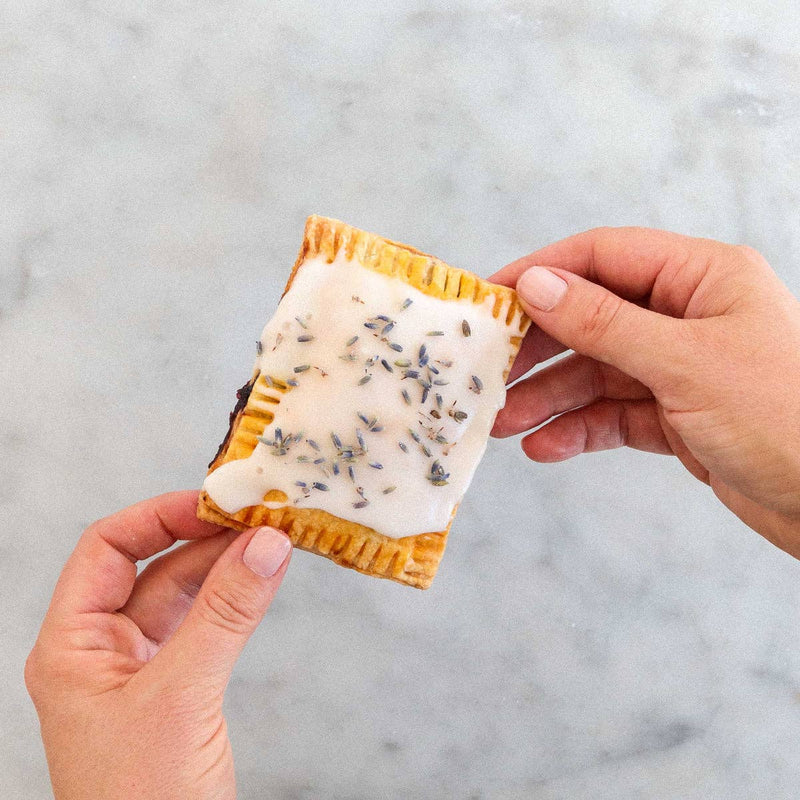 FarmSteady - Pastry Tart Making Kit: A hand-held pastry with white icing and lavender buds, held over a countertop, showcasing a nostalgic yet refined dessert.