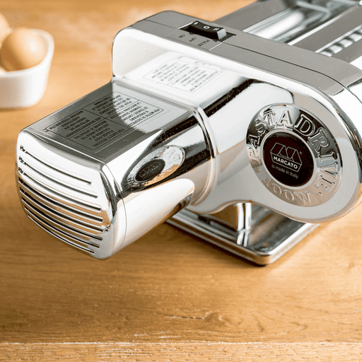 Marcato | PastaDrive Motor 110V Premium on a countertop, showcasing its chrome-plated design for easy pasta making, with a bowl and egg suggesting fresh pasta preparation.