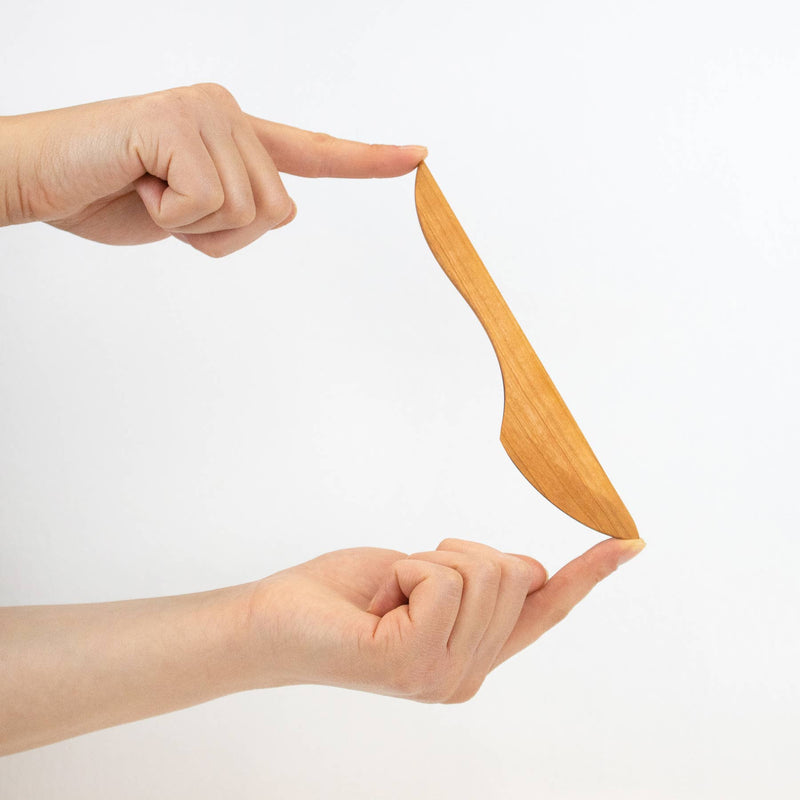 Two hands balance the Collin Garrity wooden spreader, perfect for spreading cheeses, butters, and jams, showcasing its ergonomic design for culinary use.
