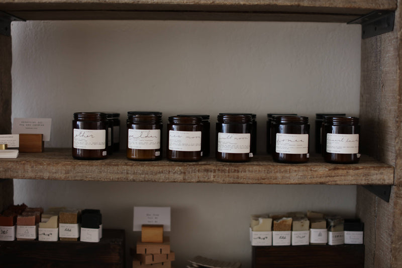 Among the Flowers - Essential Oil + Soy Wax Candle: Camp on a shelf, surrounded by similar jars, designed to repel bugs with natural essential oils.