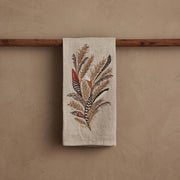 Coral & Tusk - Wheat Harvest Tea Towel featuring embroidered wheat and feathers, draped over a dowel, ideal for seasonal kitchen decor.