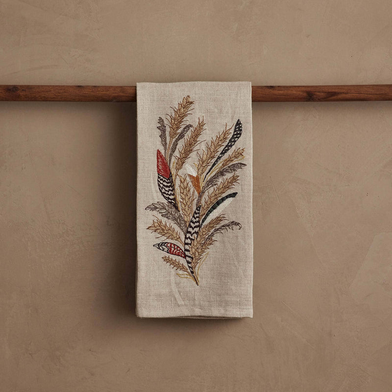 Coral & Tusk - Wheat Harvest Tea Towel featuring embroidered wheat and feathers, draped over a dowel, ideal for seasonal kitchen decor.