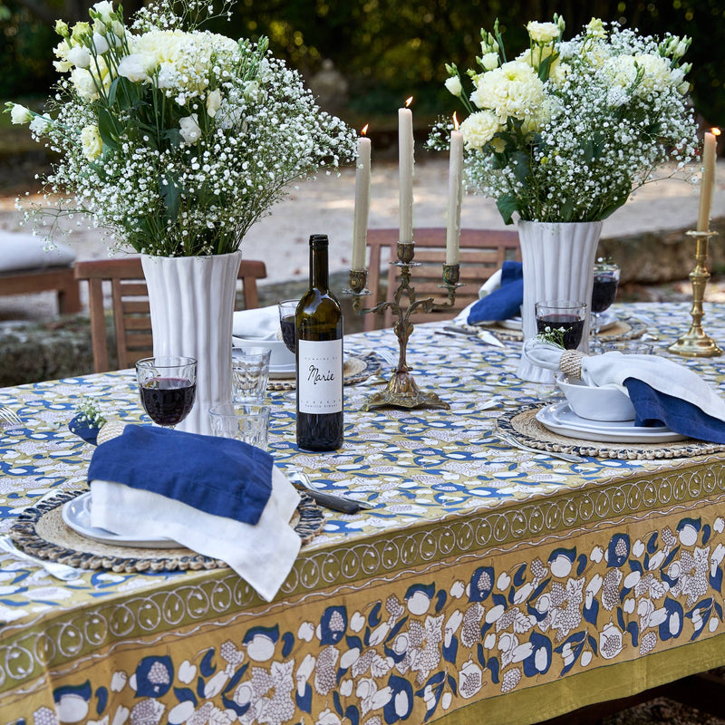 Outdoor table with Couleur Nature - Forest Harvest Mustard & Blue tablecloth, white flower vases, red wine, candelabras, and table settings, embodying Athens Cooks’ culinary elegance.