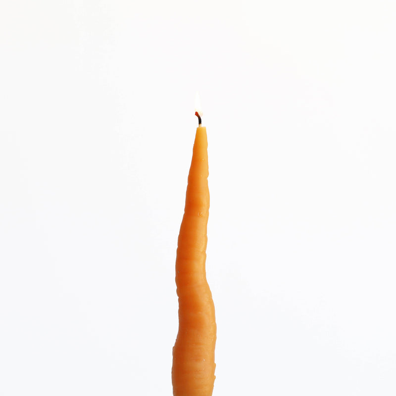 Carrot-shaped beeswax candle with a lit wick, molded from a real carrot, designed for home decor.
