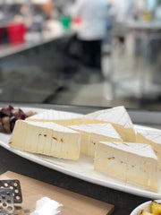 Tulip Tree Creamery - Snapdragon cheese on a platter with grapes, featuring a soft white rind and habanero peppers, displayed in a professional kitchen setting.