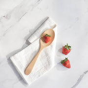 bambu® - Bamboo Serving Spoon elegantly displayed on a white linen napkin with fresh strawberries, showcasing its modern design and versatile kitchen utility.