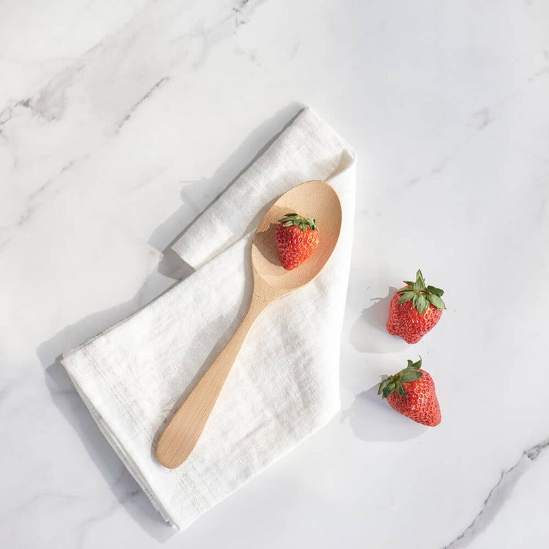 bambu® - Bamboo Serving Spoon elegantly displayed on a white linen napkin with fresh strawberries, showcasing its modern design and versatile kitchen utility.
