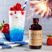 El Guapo - Bitters: Summer Berries in a bottle with sparklers, alongside a glass of blue and white drink, featuring strawberries.