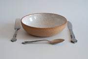RachaelPots - Pasta Bowl Small: Sage, shown in a simple setting with a metal fork, knife, and spoon, featuring a speckled white interior and earthy-brown exterior.