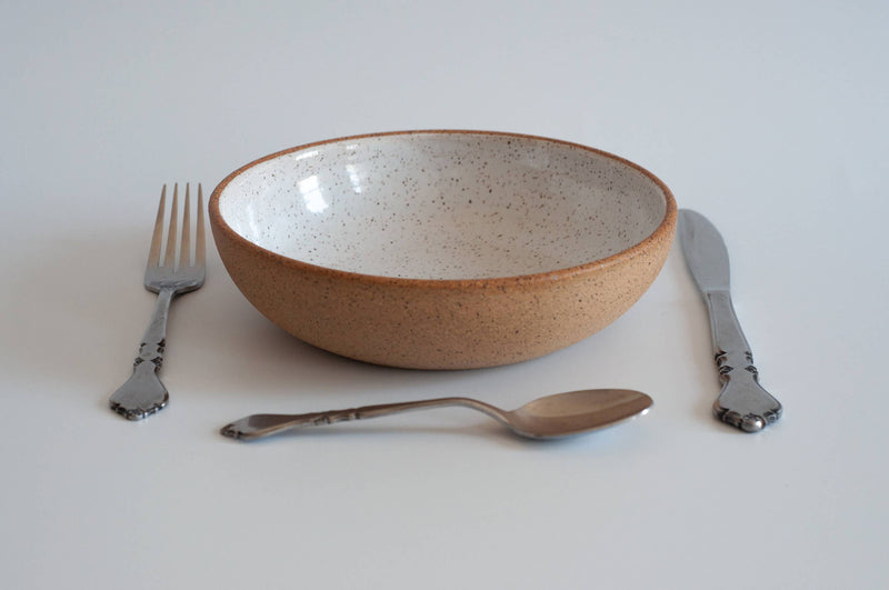 RachaelPots - Pasta Bowl Small: Sage, shown in a simple setting with a metal fork, knife, and spoon, featuring a speckled white interior and earthy-brown exterior.