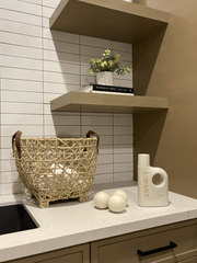 L'AVANT Collective - Wool Dryer Balls - Pack of 3 on a countertop with rattan basket, cream detergent bottle, and floating shelves with greenery and books.