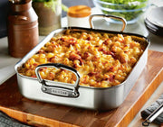 Hestan Provisions Classic Roaster with Rack, filled with baked macaroni-and-cheese, displayed on a cutting board. Ideal for versatile cooking and serving.