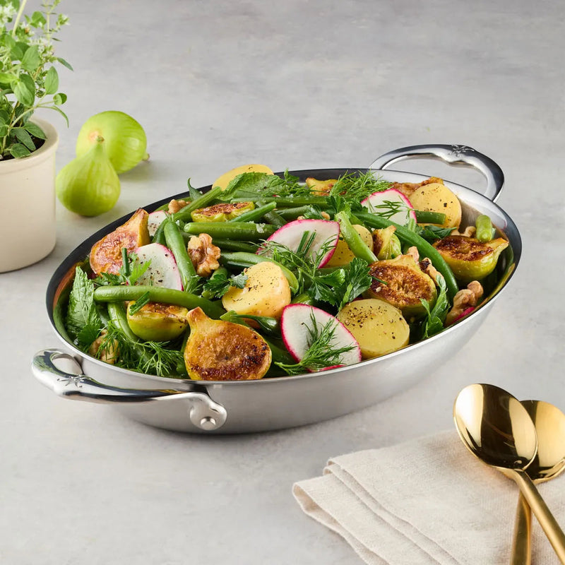 Hestan Provisions | Medium Clad Oval Au Gratin showcasing a vibrant spring salad with figs, green beans, and herbs, accompanied by elegant gold-tone serving spoons.