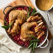 Hestan Provisions | Large Clad Oval Roaster showcasing roasted turkey parts on cranberries with herbs, featuring a small gravy saucepan, highlighting sophisticated kitchen-to-table design.