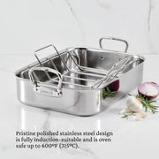 Hestan | Polished Clad Stainless Steel Roaster with Rack, Small, on marble countertop, featuring heavy-duty handles and logo, surrounded by garlic, onion, and rosemary.
