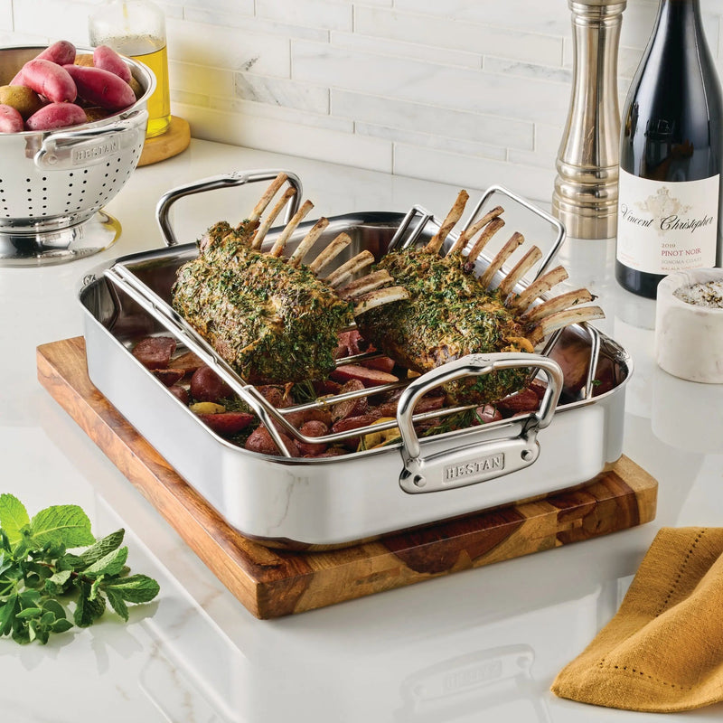 Hestan Polished Clad Stainless Steel Roaster with Rack holding herb-crusted lamb racks above roasted vegetables, showcasing craftsmanship and performance, ideal for Athens Cooks' culinary tools collection.