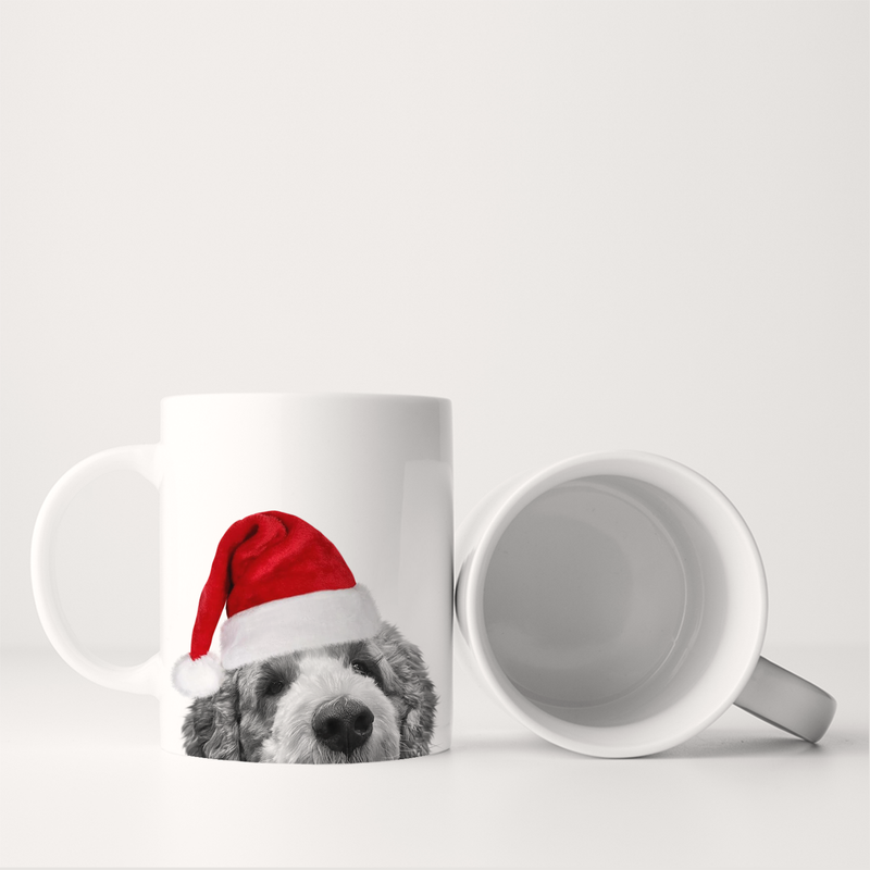 Santa Hat Doodle Mug featuring a doodle dog's face in a Santa hat, standing upright alongside an empty mug, ideal for festive sipping.