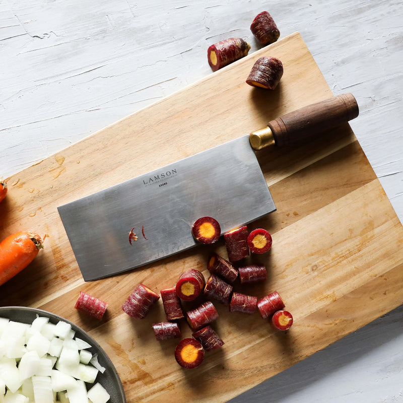 Lamson | 8 Chinese Vegetable Cleaver with Walnut Handle and Leather Sheath on a cutting board with chopped carrots and onions. Ideal for precise kitchen cutting tasks.