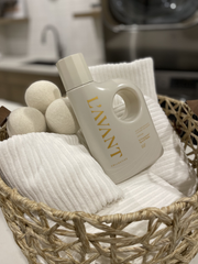 Woven wicker basket with L'AVANT Collective Wool Dryer Balls, white cotton towels, and L’AVANT detergent bottle, ideal for eco-friendly laundry care.