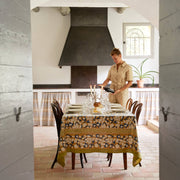 Couleur Nature - Forest Harvest tablecloth adorns a rustic dining table set for a meal, with a woman placing wine, embodying French elegance.