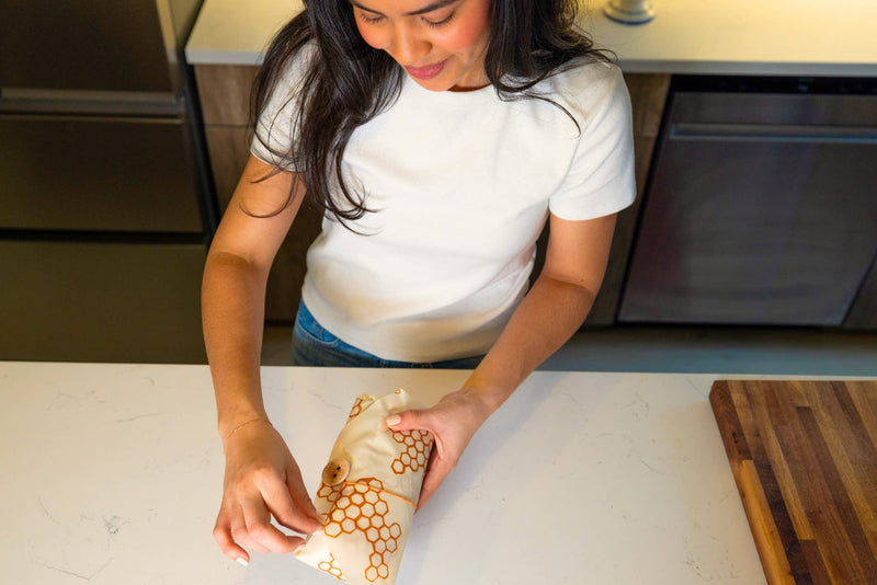 Bee's Wrap - Lunch 3 Pack - Honeycomb Print: A woman holds reusable food wraps, ideal for sustainable lunch packing with a secure button and tie closure.