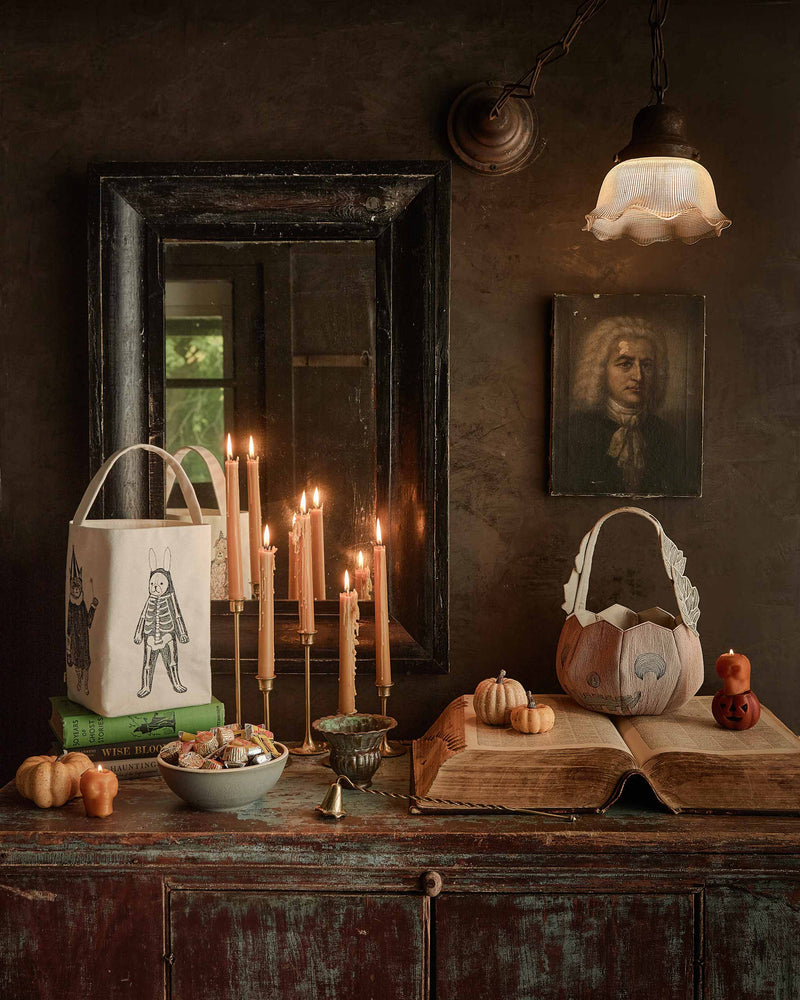 Coral & Tusk - Jack-o'-Lantern Basket amidst a vintage Halloween scene with candles, pumpkins, and books. The embroidered felt basket adds charm to traditional decor.