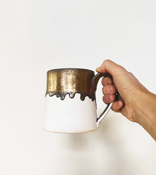 Jessica Wertz Ceramics' Gold + White Mug, featuring a handmade two-tone design with a matte white base and metallic bronze glaze, held against a light background.