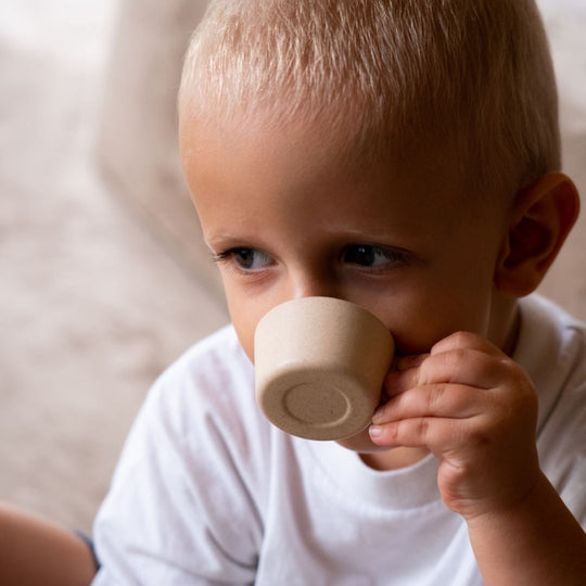 Child holding a cup from the PlanToys Pretend Tea Party Toy Set, featuring sustainably made wooden toy tea accessories for imaginative play.