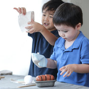 Children engaged in pretend play with the PlanToys Bread Loaf Set, featuring a sliceable bread loaf, bread knife, and baking accessories, fostering imaginative play and motor skills.