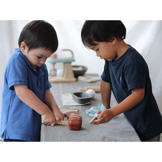 PlanToys | Bread Loaf Set: Two boys engage in pretend baking with a realistic bread loaf, tools, and accessories, fostering imaginative play and skill development.