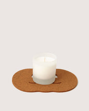 Graf Lantz - Merino Wool Pumpkin Trivet - Cumin, shaped like a smiley face, holding a white candle in a frosted glass on a brown felt coaster.