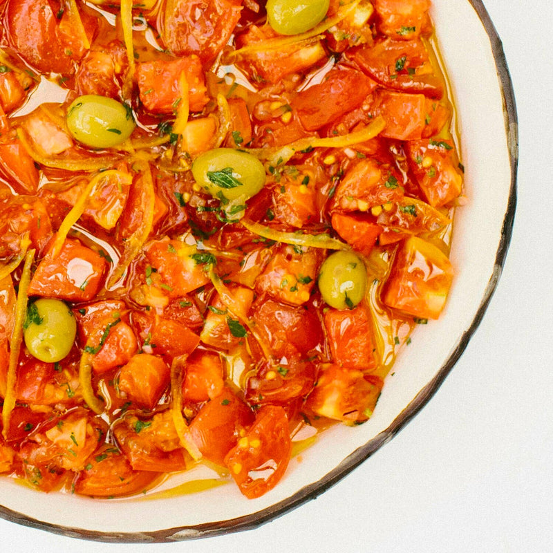 Villa Jerada - Picholine Olives - 7oz featured in a Mediterranean tomato salad with green olives, lemon zest, and fresh herbs in a white bowl.