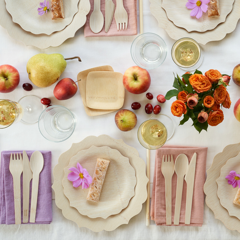 Overhead view of a styled table featuring bambu® Disposable Bamboo Knife, Fork, and Spoon Set on colored linen napkins, emphasizing eco-friendly, compostable dining options.