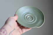 Gravesco Pottery - Handmade Pottery Spoon Rest, shown in celadon-green with a spiral pattern, held in a hand. Ideal for stovetop utensil storage.