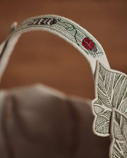 Coral & Tusk - Jack-o'-Lantern Basket handle close-up, showing felt appliqué with embroidered leaf veins and flower, reflecting a handcrafted Halloween design.