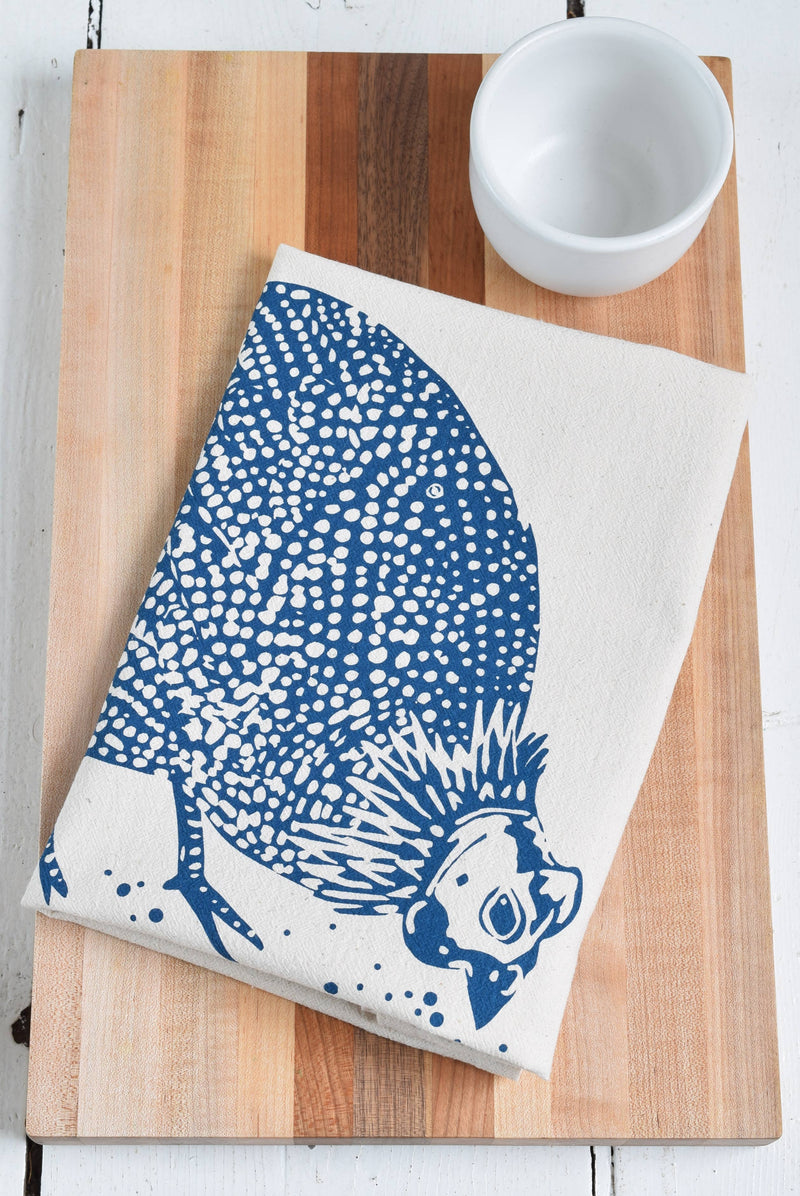 Hearth and Harrow - Organic Cotton Guinea Hen Tea Towel in Navy Blue, folded on a wooden board with a white ceramic bowl nearby, showcasing its unique bird design.