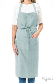 Woman wearing MagicLinen Charcoal Grey Linen Bib Apron with Pockets, showcasing its stylish and functional design ideal for cooking or gardening.