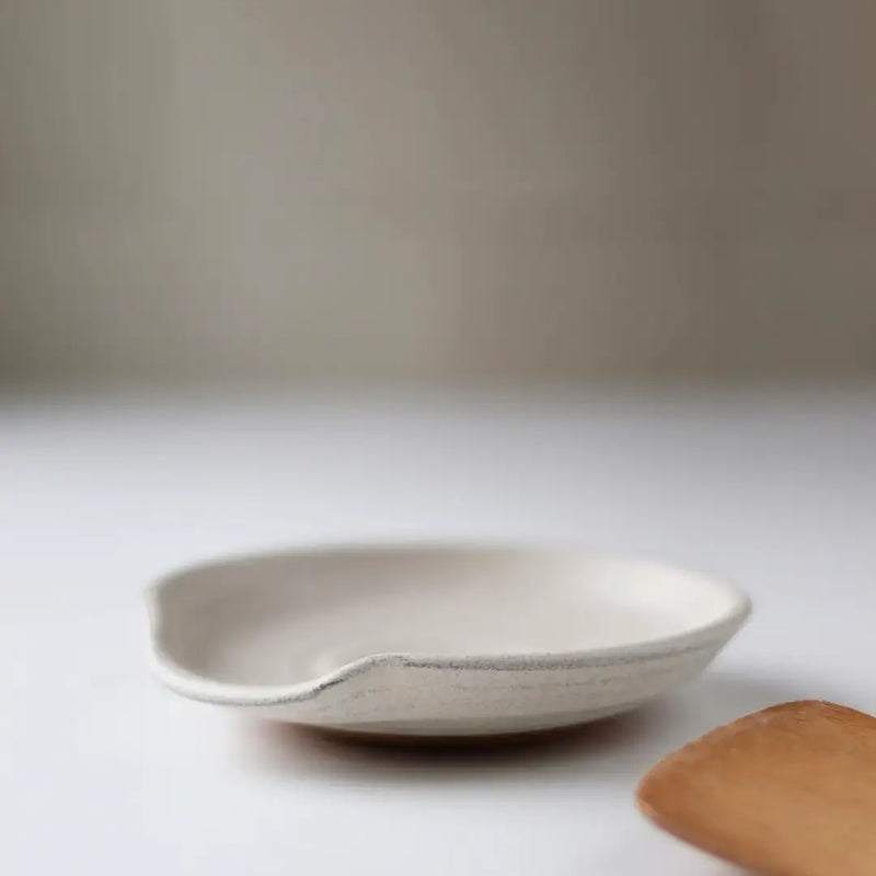 Gravesco Pottery - Handmade Pottery Spoon Rest with undulating rim, displayed on a white surface, partially showing a wooden spoon edge. Ideal for stovetops or counters.