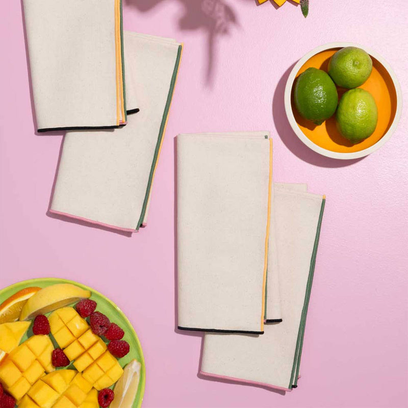 ATELIER SAUCIER - Macaw Burlap Napkins set of 4, displayed with a plate of assorted fruits and a bowl of limes on a pink surface.