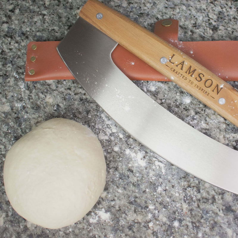 Lamson Leather Sheath for 14 Pizza Cutter/Rocker on a counter next to a dough ball and cleaver, showcasing kitchen essentials.
