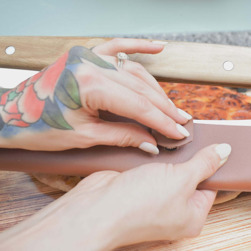 Tattooed hands holding paper, indicative of product packaging for Lamson leather sheath, designed to accompany a 14 pizza cutter/rocker.