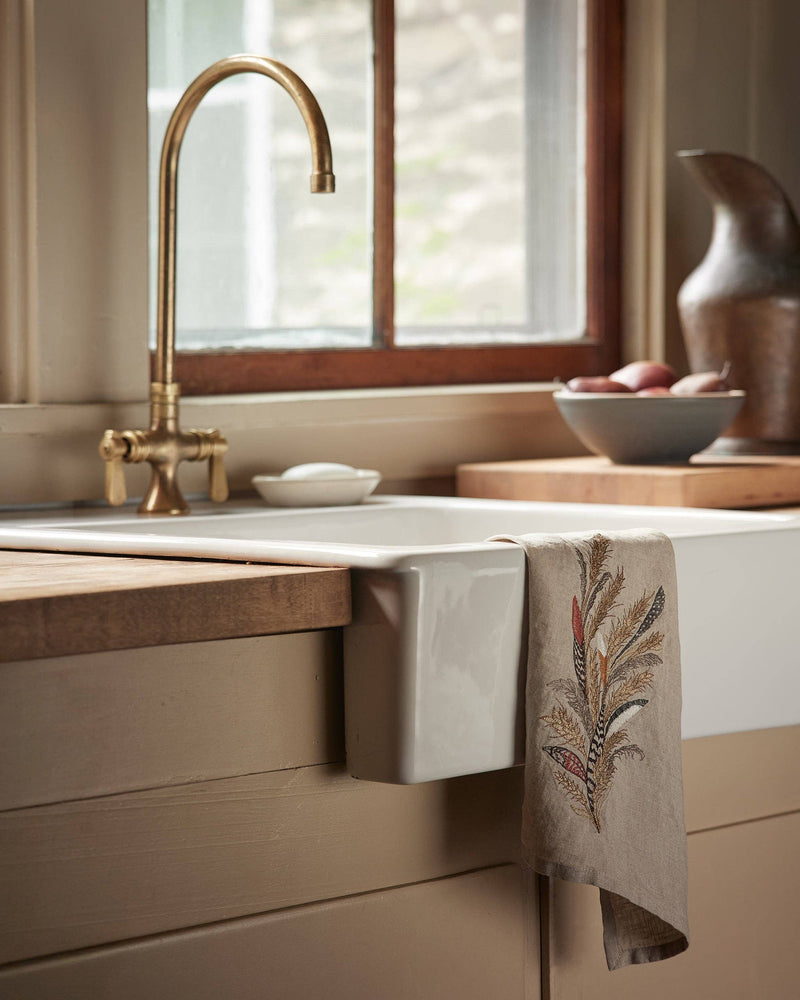 Coral & Tusk - Wheat Harvest Tea Towel draped over a farmhouse sink, showcasing embroidered grasses and grains, surrounded by rustic kitchen elements.
