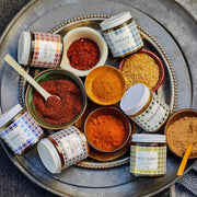 Top-down view of Villa Jerada - Dukkah - 50g in a bowl on a tray with various spice blends, featuring small spoons for scooping.